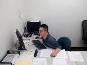 This is a photo of a young adult male sitting at a desk looking at a computer screen who is mentally challenged but showing his skills.
