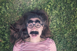 Woman wearing a funny Groucho Marks mask, laying in the grass.